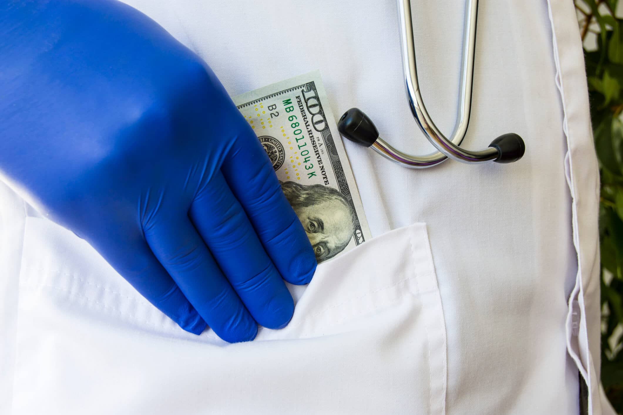 gloved hand putting cash in pocket of medical coat